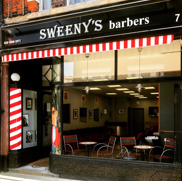The shopfront of Sweeny&rsquo;s Barbers at 7 Bond Street, Ealing, with its black fascia and red-and-white striped awning.